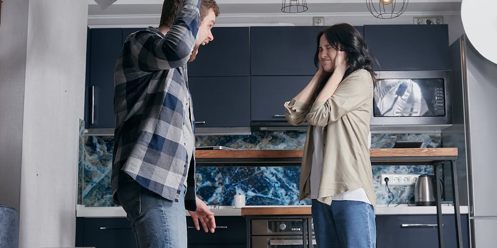 An image of a worried parent sitting at a kitchen table with bills and a laptop open, looking at a legal notice about child support. The background should have a child’s drawing on the fridge, representing the emotional impact of financial struggles on family life.