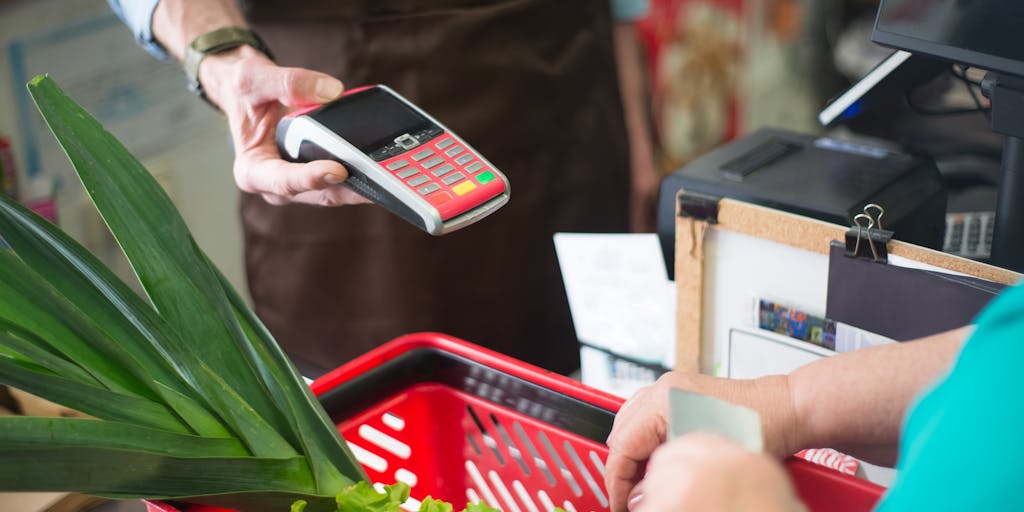 A close-up of a hand holding a food stamp card with a background of a grocery store aisle filled with fresh produce. The focus on the card signifies empowerment and the ability to access resources, while the vibrant colors of the produce represent hope and nourishment.
