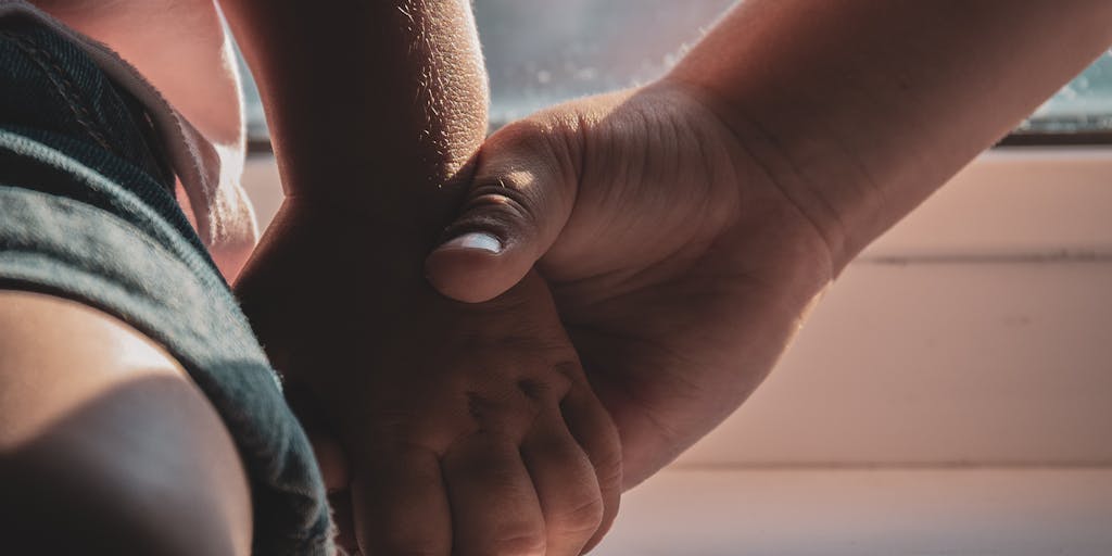 A close-up shot of a mother and child holding hands, with a shadow of a gavel in the background, representing the legal implications of child support decisions. The lighting should be warm to convey a sense of love and protection.