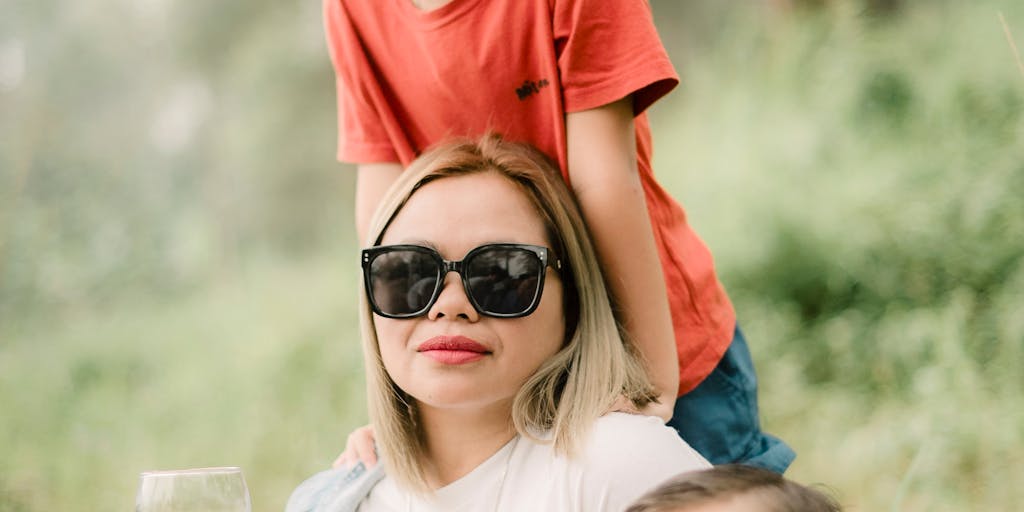 An outdoor scene where a mother and child are sitting on a park bench, with a thought bubble graphic above the mother’s head filled with symbols of money, law, and family. This represents her thoughts on child support.