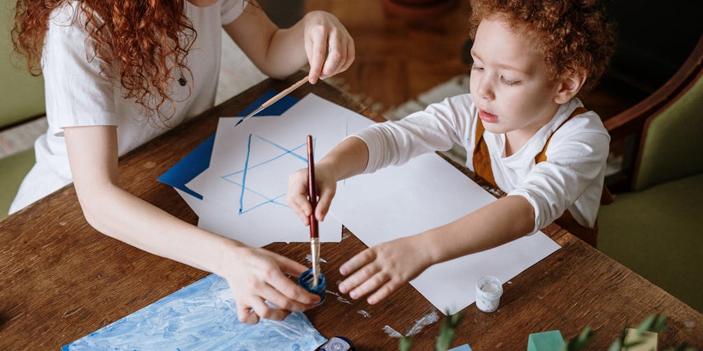 A close-up shot of a hand holding a 'Stop' sign made of paper, with a child’s drawing in the background. This image represents the idea of taking control and making decisions regarding child support, with a focus on the child's perspective.