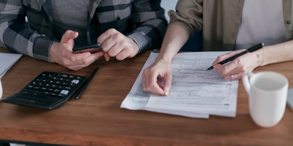An overhead shot of a family sitting around a dining table with a laptop open, discussing finances. The laptop screen displays a tax form with a highlighted section about child support. This captures the intersection of family life and financial responsibilities.