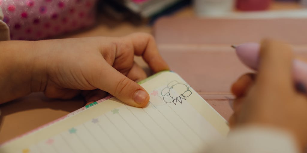 A close-up shot of a child's drawing on a piece of paper, depicting a house with a sad face and a broken heart. The drawing is surrounded by crumpled bills and a calculator, symbolizing the financial strain and emotional toll on children when child support is not paid.
