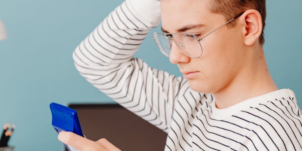 A thoughtful teenager sitting at a desk, reviewing financial documents with a calculator and a laptop open, symbolizing the responsibility of managing their own finances as they approach adulthood. The room is filled with personal items that reflect their interests, showcasing their transition into independence.