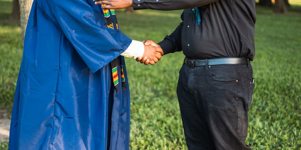 A close-up shot of a pair of hands, one belonging to a parent and the other to a young adult, shaking hands. This symbolizes the transition from dependency to independence, highlighting the end of child support as the young adult steps into adulthood.