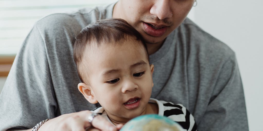 A close-up of a globe with a child's hand pointing to one country and a father's hand pointing to another, representing the geographical separation and the legal challenges of obtaining child support across borders.